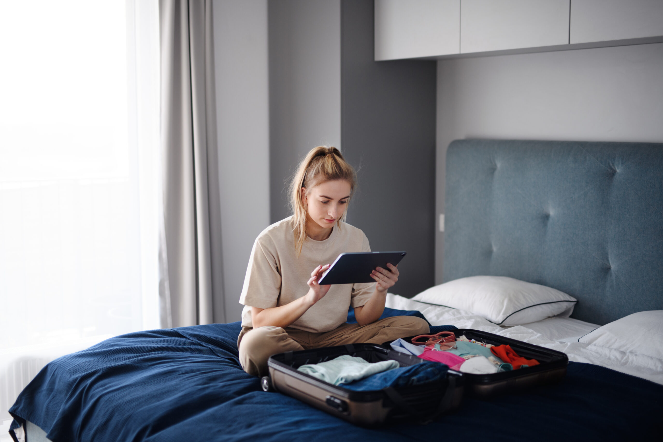 Creating a Travel Itinerary - Portrait of young woman sitting on bed indoors at home, planning holiday